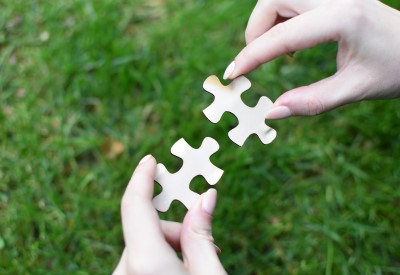 Two jigsaw pieces being held close together over green grass